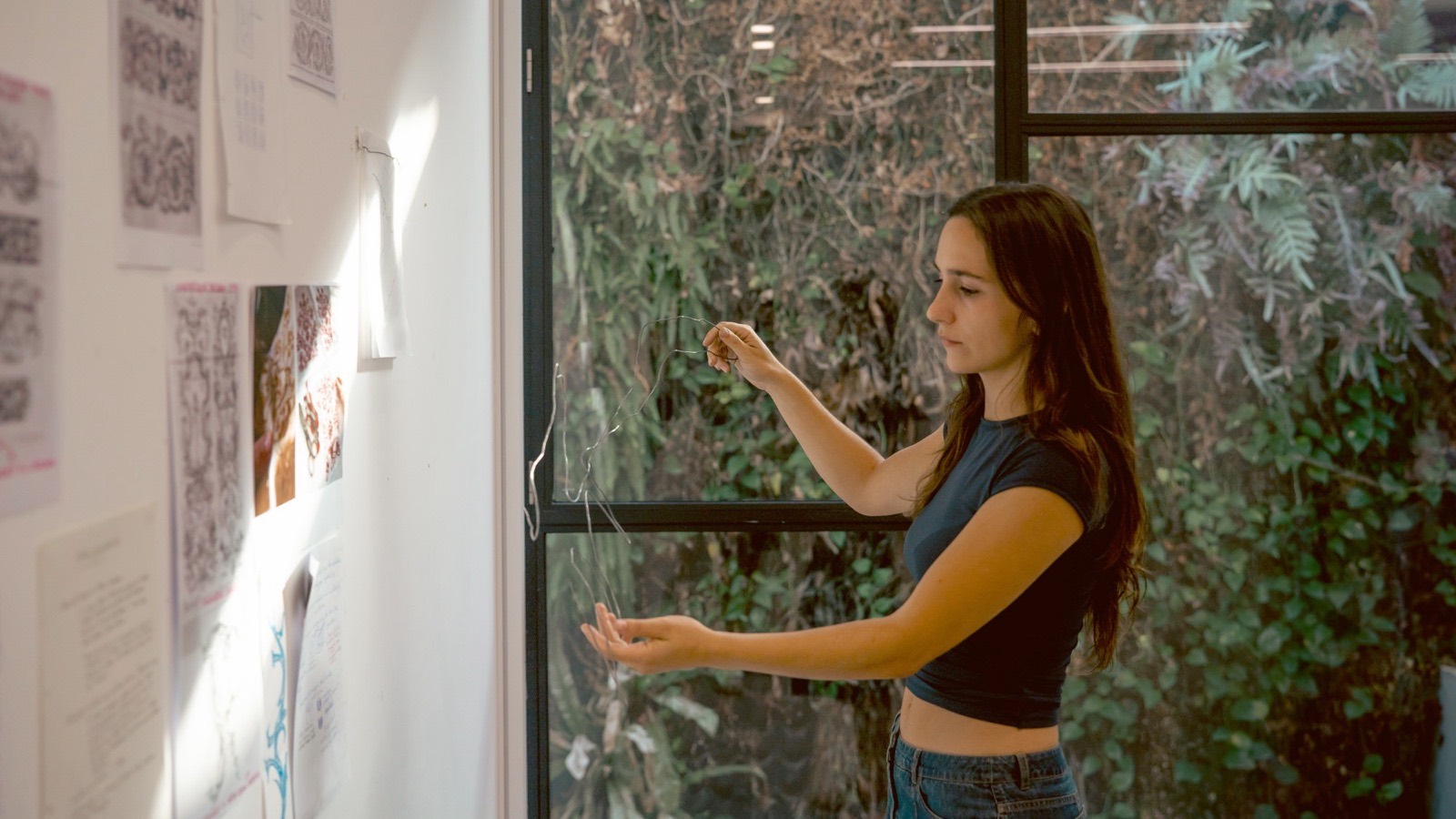 Blanca Tejerina trabaja con un alambre junto a una ventana, frente a una pared con dibujos